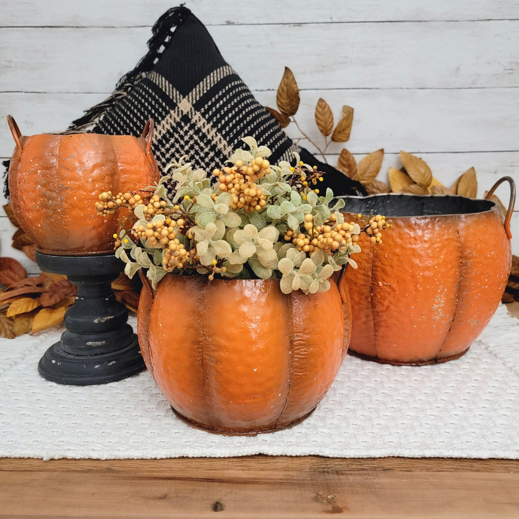 Rustic autumn vignette of 3 orange metal pumpkin containers with a sage green floral orb.