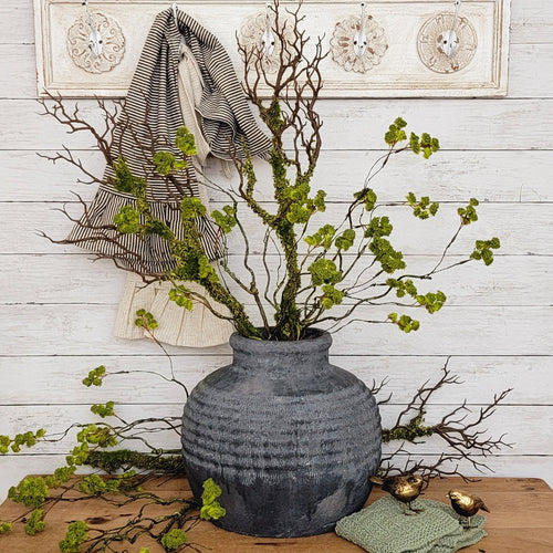 Rustic black terracotta vase with mossy branches.