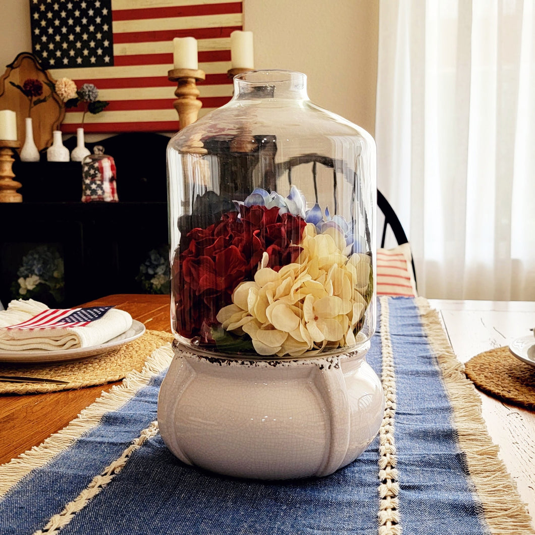 Patriotic hydrangea centerpiece in a glass and ceramic terrarium with a denim table runner.