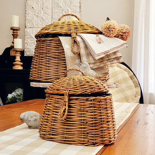 Natural wicker hut baskets with hunged lids displayed as a neutral centerpiece with a tan buffalo check table runner in a cottage farmhouse kitchen.