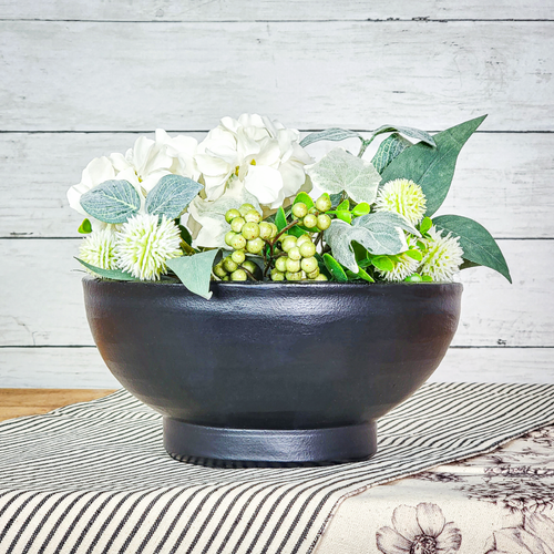 Matte black ceramic bowl table decor with an artificial white hydrangea with green foliage half orb setting on top of a black and white ticking stripe table runner