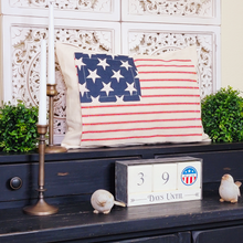 Load image into Gallery viewer, Antique style brass candle holder displayed in front of architectural wall decor vintage style American flag pillow boxwood orbs holiday countdown and weathered bird figurines
