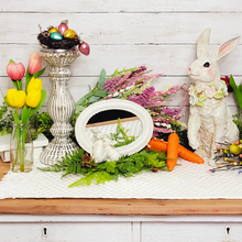 Load image into Gallery viewer, Spring and Easter side table display featuring pink and yellow tulips in glass vases, a frosted mercury glass pillar candle holder with a birds nest displayed on top filled with pastel glass miniture ornaments. Artificial greenery and fux spiked lavender flowers behind a chippy white oval tabletop mirrow with small bunnies peeking in and a large resin rabbit with pastel floral ring around its neck.
