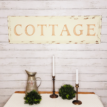 Load image into Gallery viewer, Large vintage chipped paint and distressed wood carved cottage wall decor sign hung on a shiplap wall above a sidetable displaying faux boxwood half spheres, a rustic bee embossed metal pitcher, and copper metal taper candle holders.
