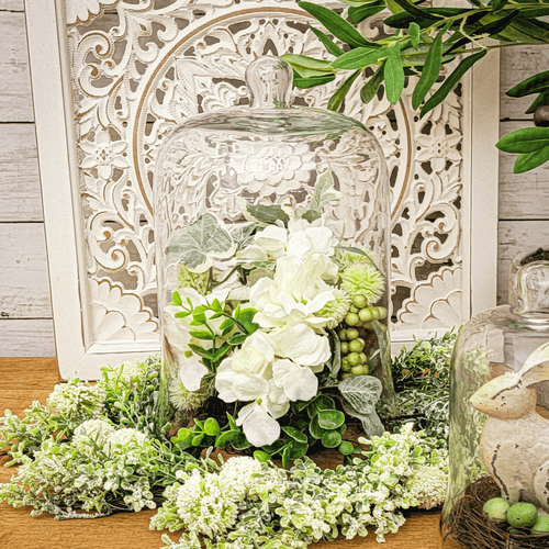 Glass chloche filled with white hydrangea and green foliage.