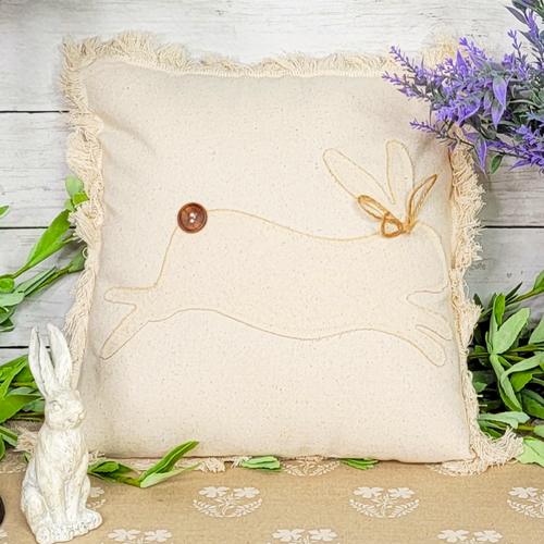 Linen colored 12 inch throw pillow with fringe edging and a patchwork bunny. 