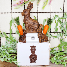 Load image into Gallery viewer, three faux chocolate Easter bunnies small medium and large displayed on top of an antiqued handle drawer container and white tinket box with crystal knob
