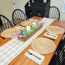 Load image into Gallery viewer, Spring tablescape with a tan and linen buffalo plaid table runner chipwood rectabgle basket with pink and lavender artificial flowers in it with flameless candles round jute placemats and gingham napkins
