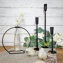 Load image into Gallery viewer, Glass Bottle Stem Vase in a Metal Stand pictured with Hand Forged Black Iron Taper Candle Holders, Weathered Resin Bird Figurines setting on a Black and White Tocking Stripe Reversible Table Runner and artificial white hydrangea and green foliage pick
